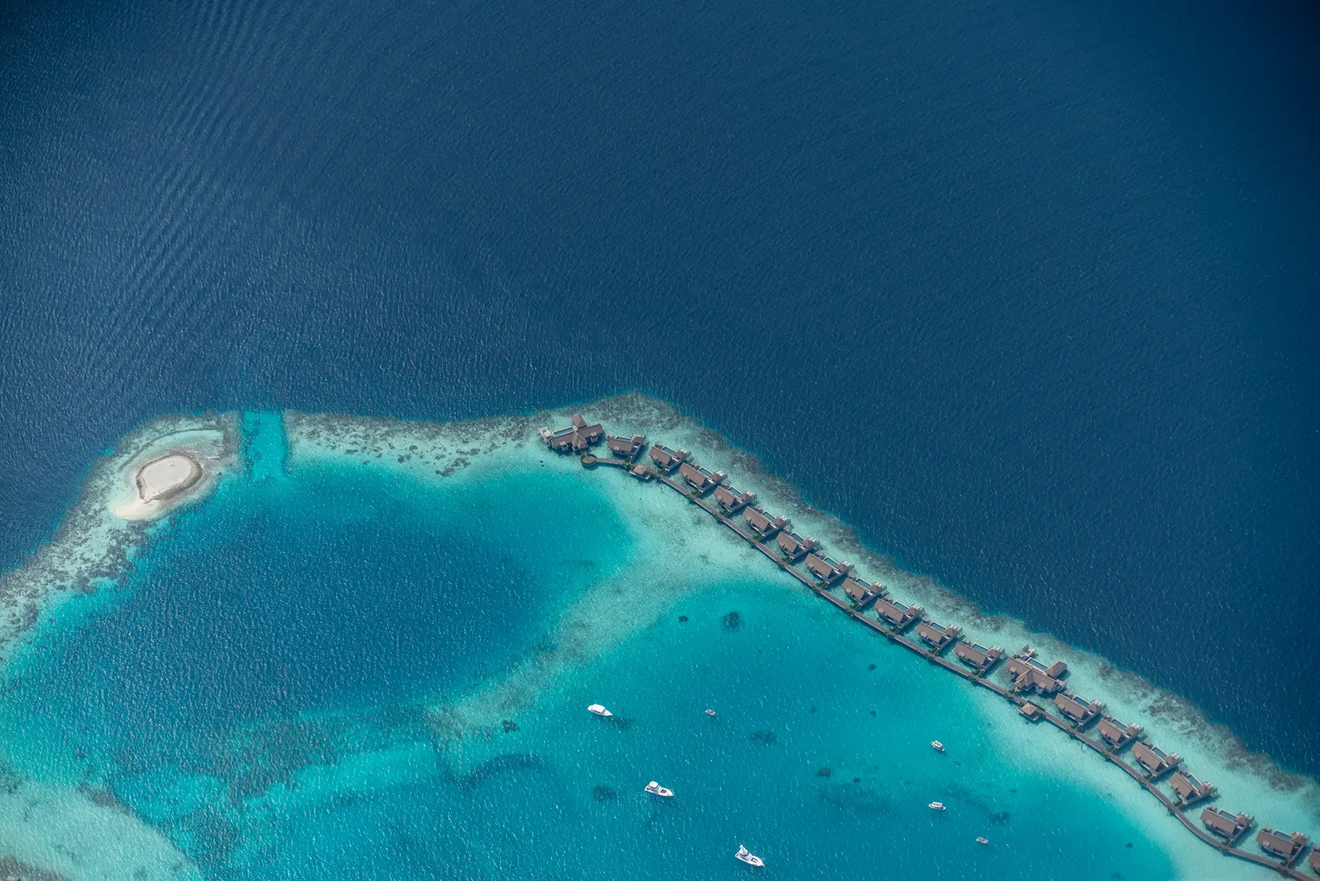 Maldivian water villa pier seen from above with beautiful blue ocean north of the pier and light blue water south of it over the reef